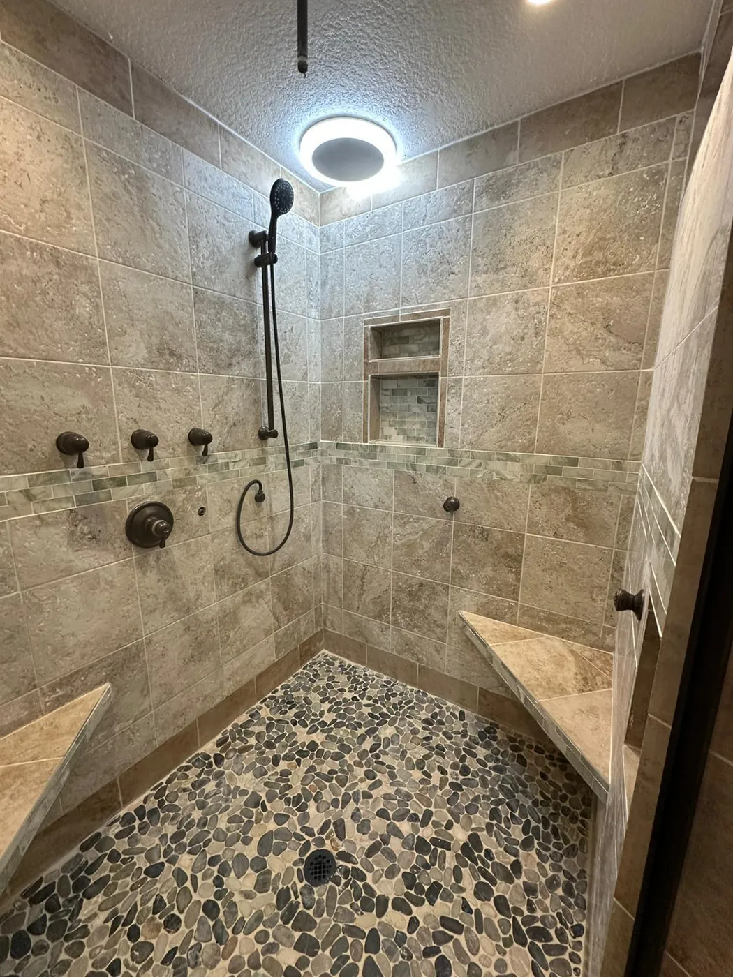 Walk-in shower with a pebble floor, rain head and a lit niche.