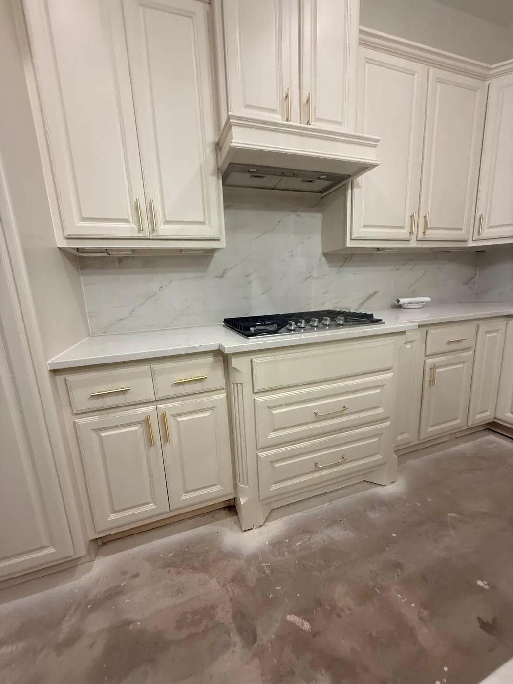 Cream cabinets with a marble backsplash, hood and cooktop installed.